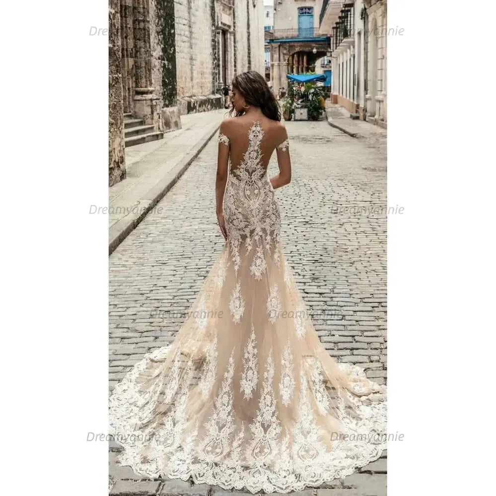 Champagne mermaid wedding dress with off-the-shoulder neckline, intricate lace applique, and a floor-length tulle train.