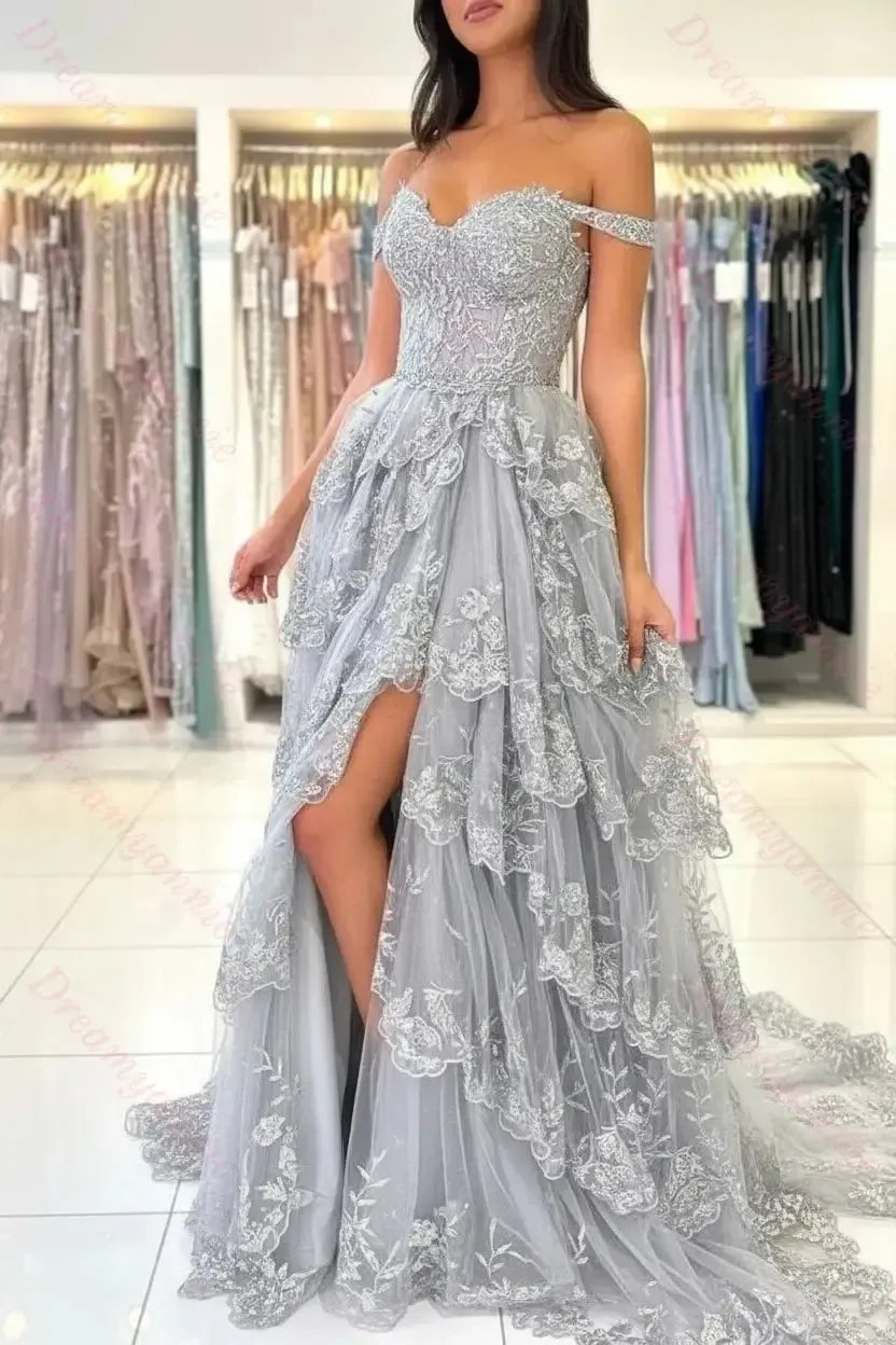 Off-the-shoulder ivory lace wedding dress with a tiered tulle skirt, sweetheart neckline, and a high side slit.
