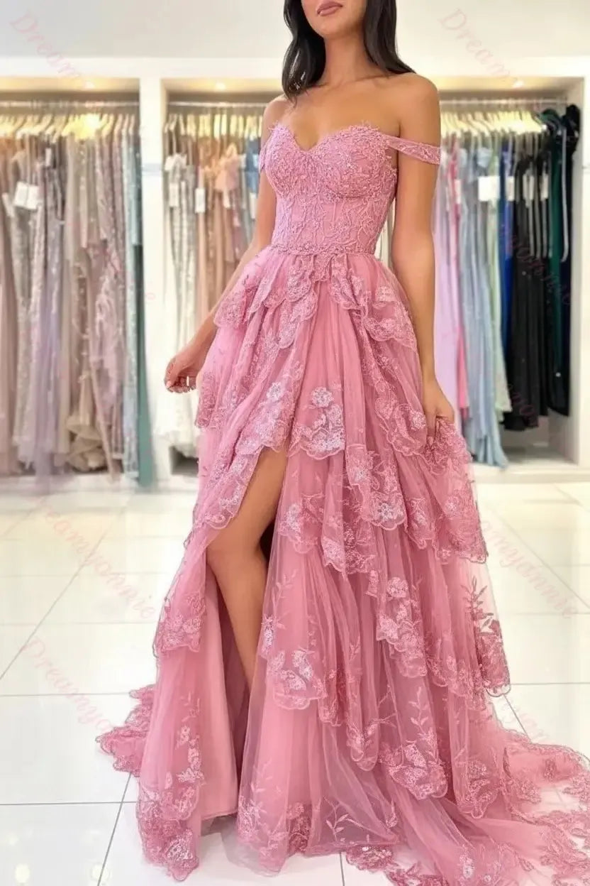 Dusty rose off-the-shoulder bridal gown featuring tiered lace, tulle layers, and a high-slit skirt in a boutique setting.