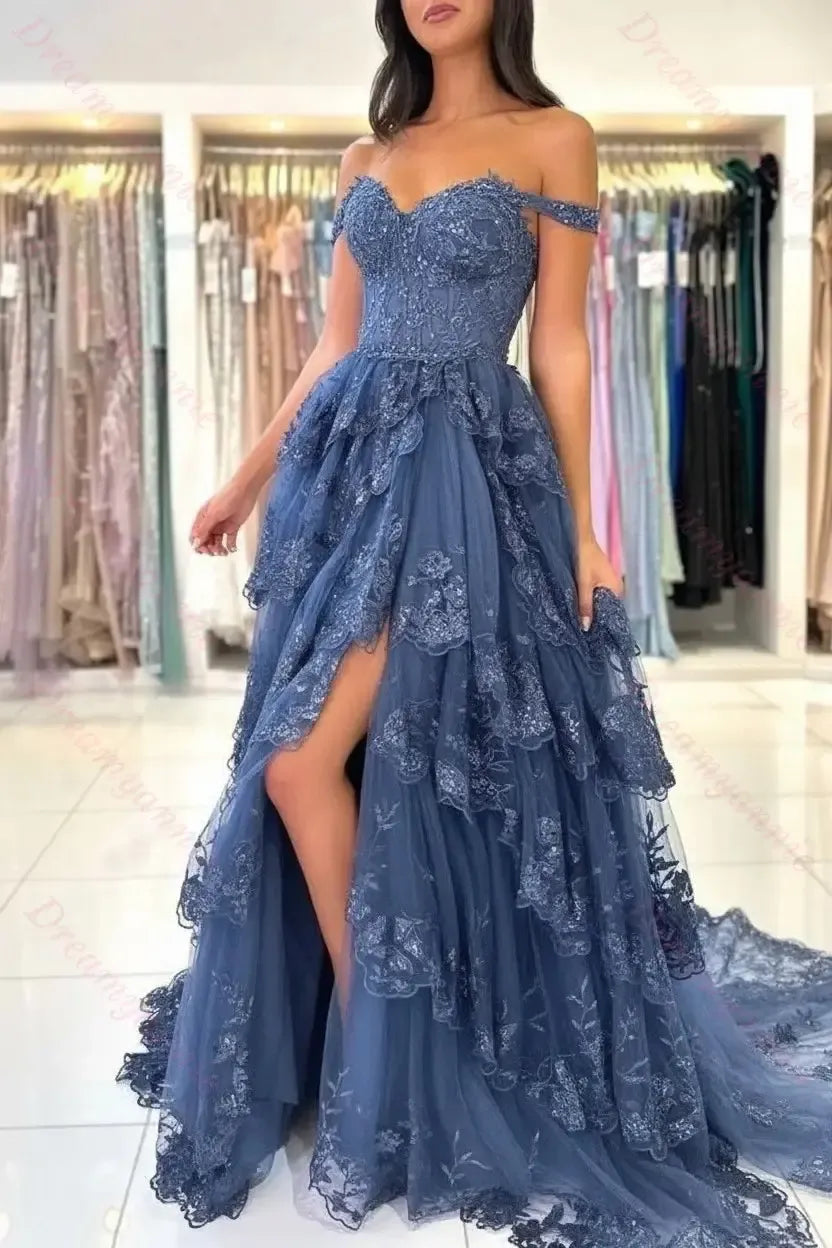 Dusty blue off-the-shoulder bridal gown featuring tiered lace, tulle fabric, and a high leg slit in a boutique setting.